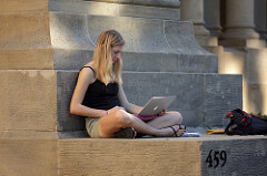 Junge STudentin sitzt mit Laptop vor der Uni.